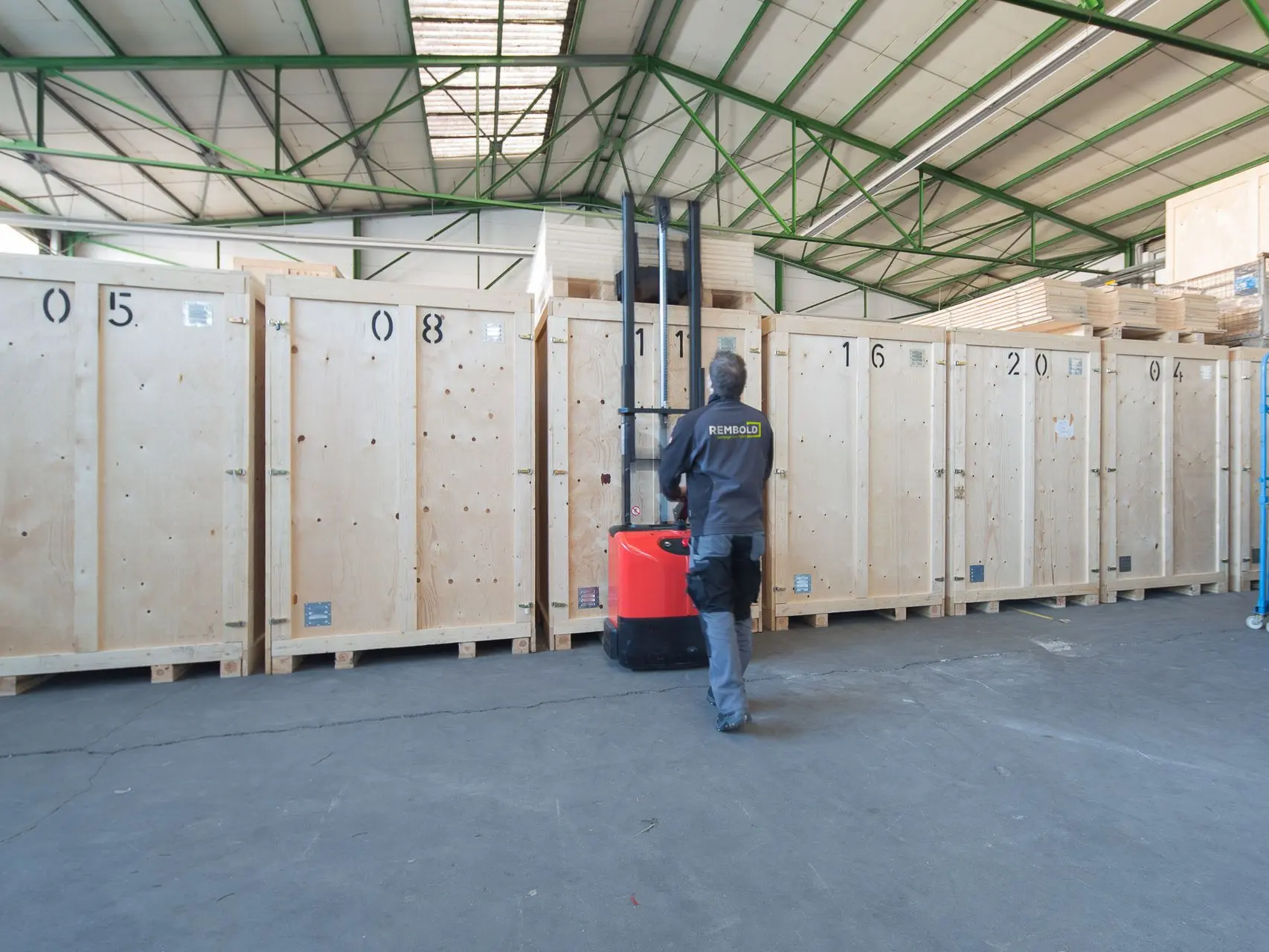 In a warehouse a REMBOLD employee is moving a large storage box with a pallet truck..
